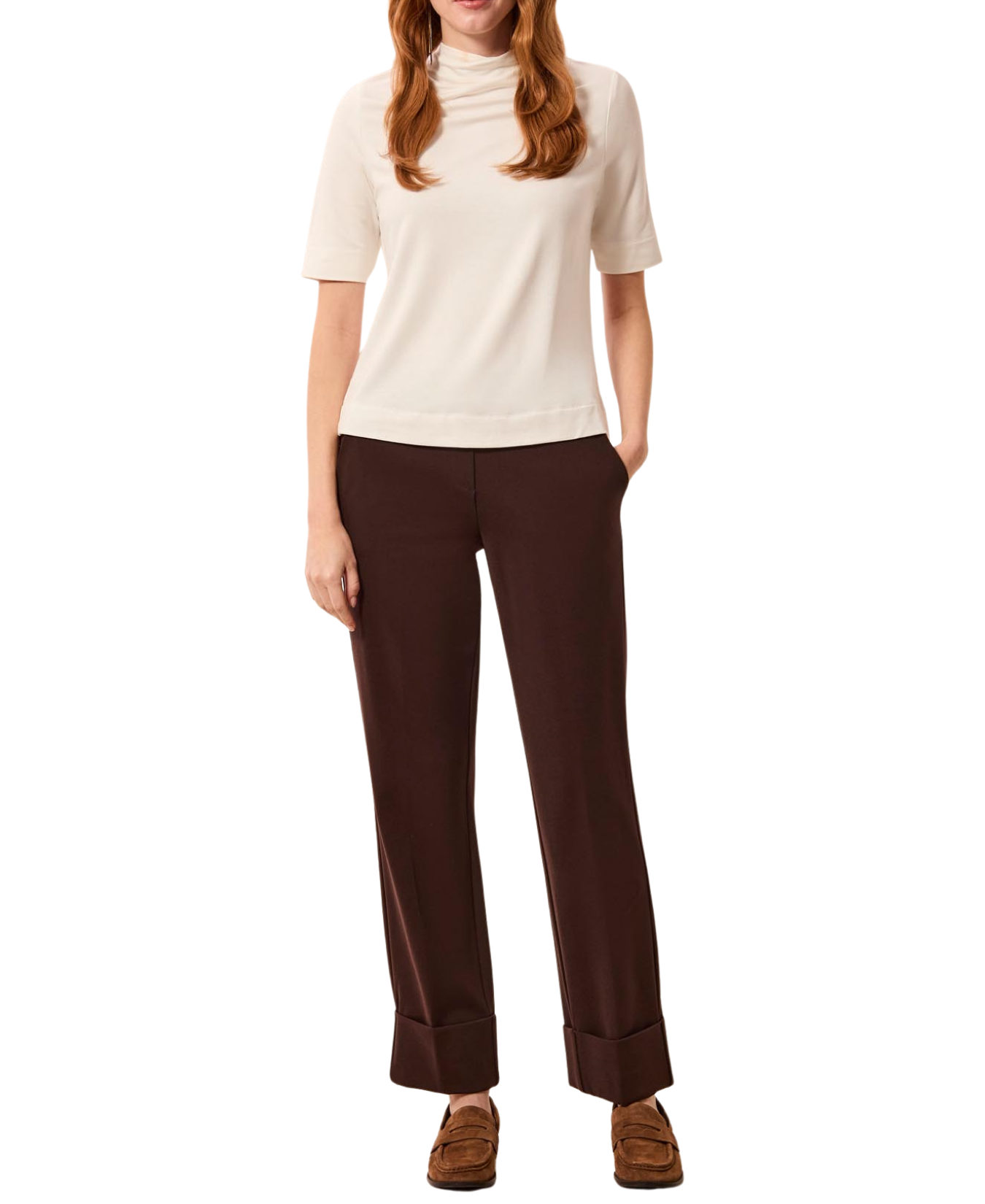 a woman with red hair wearing a white shirt and brown pants