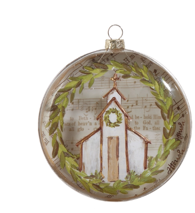 a glass ornament with a painting of a church and a wreath